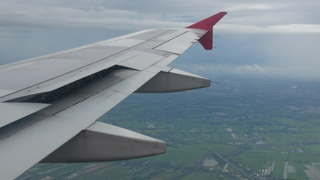 view through aircraft window with plane's wing over green farm field site suburb of Bangkok area while plane is landing