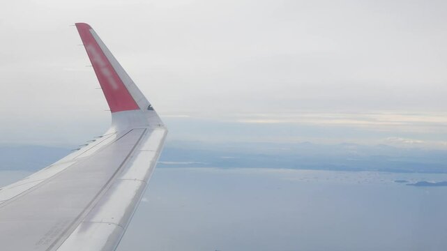 view through plane window from inside airplane cabin while climbing flying over the sky with airplane wing winglet and fluffy cloud outside