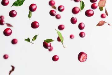 Fresh cranberries and leaves on a clean white surface, perfect for food or nature photography