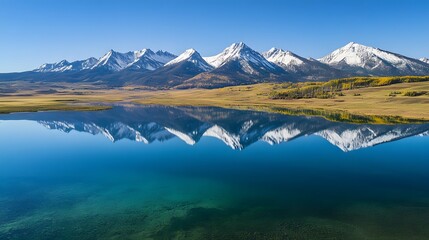 Naklejka premium Scenic mountain reflection over calm lake, serene natural landscape showcasing blue sky and snow-capped peaks, tranquil atmosphere.
