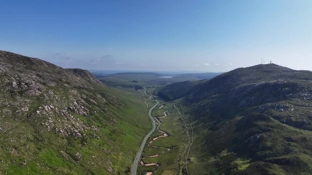 Barnesmore Gap, County Donegal, Ireland, June 2023. Drone pushes forwards in a panoramic vista above the valley with shadows covering the wild landscape as the N15 road and river navigate the pass.