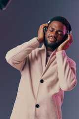 A joyful man enjoying music with closed eyes, wearing a stylish beige coat and headphones,...