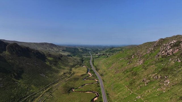 Barnesmore Gap, County Donegal, Ireland, June 2023. Drone pushes forward and ascends to a panoramic overview following the gentle curves of the N15 road through the valley with a meandering river.