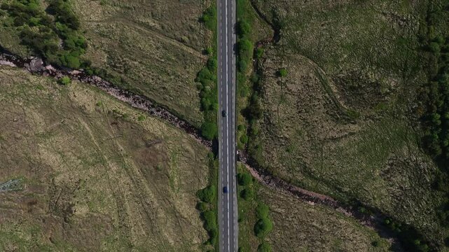 Barnesmore Gap, County Donegal, Ireland, June 2023. Drone in Bird&rsquo;s Eye View pulls backwards above the road with bridges over river as cars navigate the route with winding streams and exposed rocks.