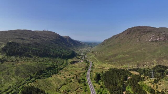 Barnesmore Gap, County Donegal, Ireland, June 2023. Drone pushes forwards in a panoramic wide establishing view to the entrance of the mountain pass following the N15 road next to a meandering river.