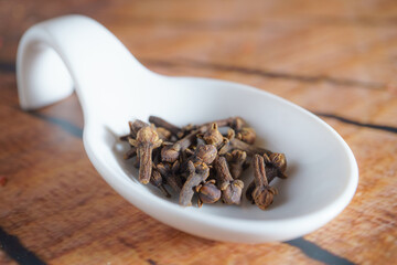 white ceramic spoon with clove seeds on a wooden table and copy space