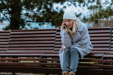 Smiling young woman walking through a frosty city street on a winter morning, talking on her...