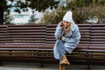 Smiling young woman walking through a frosty city street on a winter morning, talking on her...