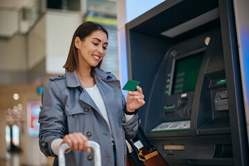 Happy traveler using her credit card at ATM at the airport.