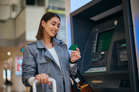 Happy traveler using her credit card at ATM at the airport.