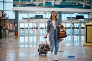 Happy woman pulling her suitcase while walking through airport hallway.