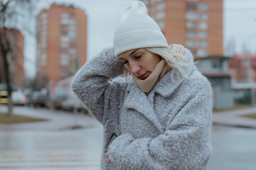 Smiling young woman walking through a frosty city street on a winter morning, talking on her smartphone. She wears a gray coat and a warm hat, radiating joy and positive emotions in the chilly urban s