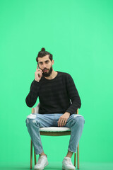 A man, full-length, on a green background, sitting on a chair