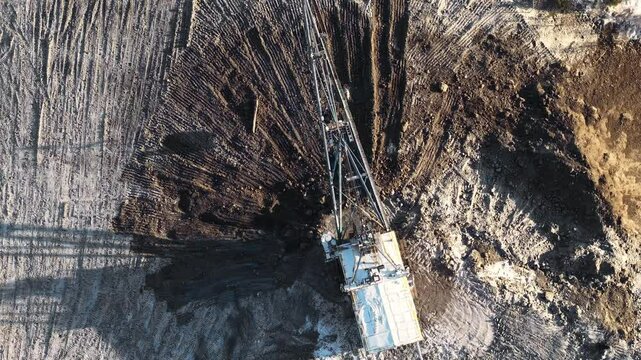 Aerial view of excavator digging in open pit coal mine revealing layers of earth and minerals, mining industry.