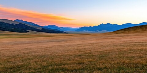 Obraz premium A serene landscape showcasing rolling hills, golden grasslands, and a colorful sunset sky over distant mountains.