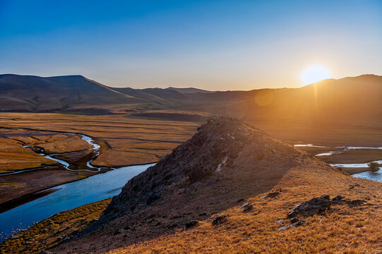 Sonnenauf- oder Untergang hinter einem Bergr&uuml;cken &uuml;ber einem menschenleeren Flusstal in der Steppe der Mongolei, Asien