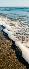 A close-up view of gentle ocean waves lapping onto a sandy beach, highlighting the textures of sand and foam against a serene backdrop.
