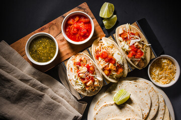 Overhead view of delicious tacos arranged next to cups of salsa on a rustic table. Vibrant...