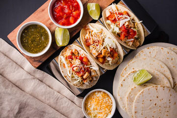 Overhead view of delicious tacos arranged next to cups of salsa on a rustic table. Vibrant ingredients like fresh cilantro, diced onions, and zesty lime wedges add color and texture.