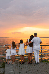 Fototapeta premium Happy family of five is standing on pier overlooking the ocean and enjoying the view and taking in the peaceful atmosphere