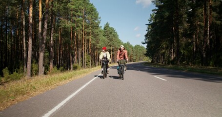 Naklejka premium A young couple is riding a bike on a road in the middle of the forest. Active leisure on a sunny day