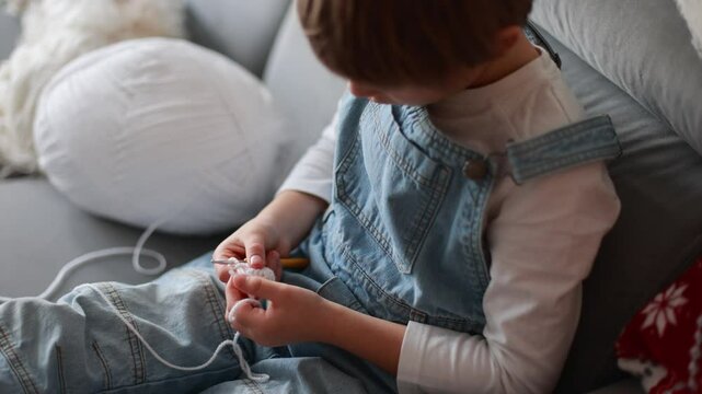 Child, learning crocheting, knitting, hand Crochet basics. Kid sitting at home, crocketing amigurumi figure