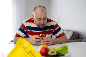A man sits quietly, contemplating his food choices, carefully balancing between healthy and...