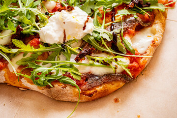 Culinary Delight of a Fresh Artisanal Pizza Topped With Creamy Burrata, Sun-Dried Tomatoes, and Vibrant Arugula Served in a Cozy Kitchen Setting