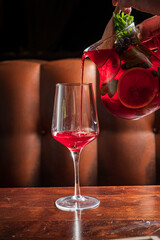 Refreshing Summer Beverage Being Poured Into a Crystal Wine Glass With a Rich Wooden Table Seen in an Inviting Lounge Setting at Sunset
