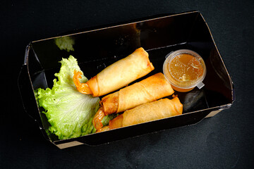 Deliciously Crispy Spring Rolls Served With a Tangy Dipping Sauce, Nestled on Fresh Lettuce Leaves in a Sleek Black Takeout Box
