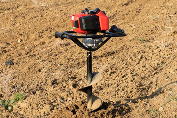 An earth auger machine opreated for digging holes to install fence posts at the edge of a field