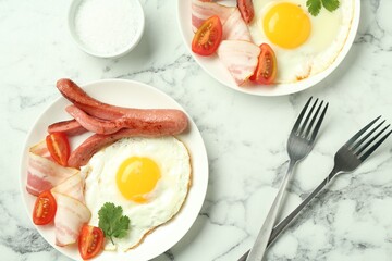 Tasty brunch. Fried eggs, sausage, bacon and tomatoes served on white marble table, flat lay