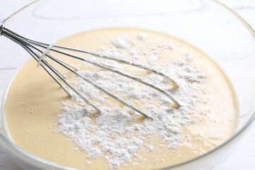 Whisk and glass bowl of dough, closeup