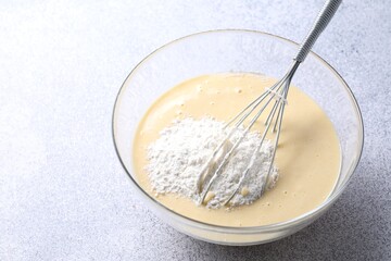 Whisk and bowl of dough on grey table, closeup. Space for text