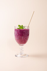 Blueberry milkshake in cut crystal glass with beige straw and fresh mint on neutral background. Copy Space. Elegant and natural presentation. Concept of healthy eating, freshness and wellness