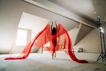 Ballerina in red fabric leaping gracefully, fabric resembling wings