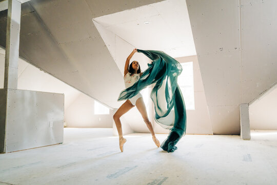 Ballerina dynamically posing with flowing green fabric in a loft