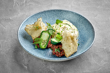 A vibrant and appetizing plate of beef tartare, served with fresh herbs, crispy crackers, and a dollop of creamy sauce