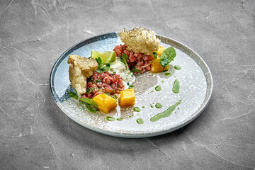 A vibrant and appetizing plate of beef tartare, served with fresh herbs, crispy crackers, and a dollop of creamy sauce