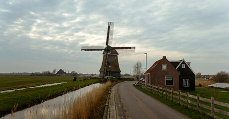 Traditional Dutch windmill standing tall beside a rural road under an overcast sky in the flat polder landscape