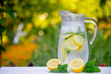 Glass of lemonade with lemons and fresh mint, on a light background in the garden.