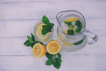 Glass of lemonade with lemons and fresh mint, on a light background in the garden.
