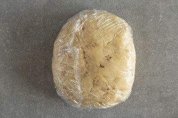 Kneaded scone dough in plastic wrap on a grey background.
