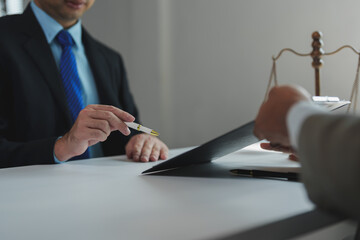 Lawyer holding a pen and pointing at a document during a meeting with a client, with scales of...