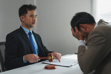 Asian lawyer holding gavel and explaining verdict to stressed businessman in courtroom or office, legal advice, consultation, and judgment concept