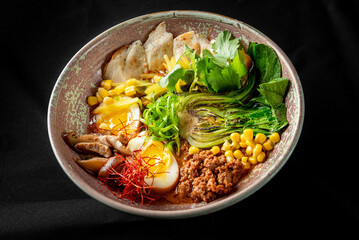 A beautifully arranged bowl of ramen featuring tender slices of meat, soft boiled eggs, fresh greens, corn, and vibrant garnishes, set against a dark background for contrast.