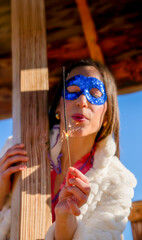 Woman wearing a blue mask with a party dress blowing a sparkler outdoors during a birthday party to...