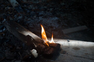 Bright flames ignite on a wooden base among scattered stones, highlighting the charm of fire in the...