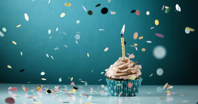Confetti Fall on Cupcake with one candle on top, captured in super slow-motion on teal backdrop. Birthday anniversary concept celebration