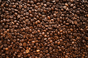 Background of freshly roasted coffee beans. A close-up top view texture of aromatic brown coffee beans. Coffee production. Brewing. Perfect for cafe, coffee shop, and beverage industry concepts.